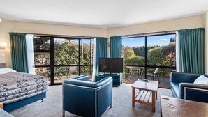 Hotelkamer met een bed, een sofa, een televisie en een balkon met uitzicht op bomen en bergen.