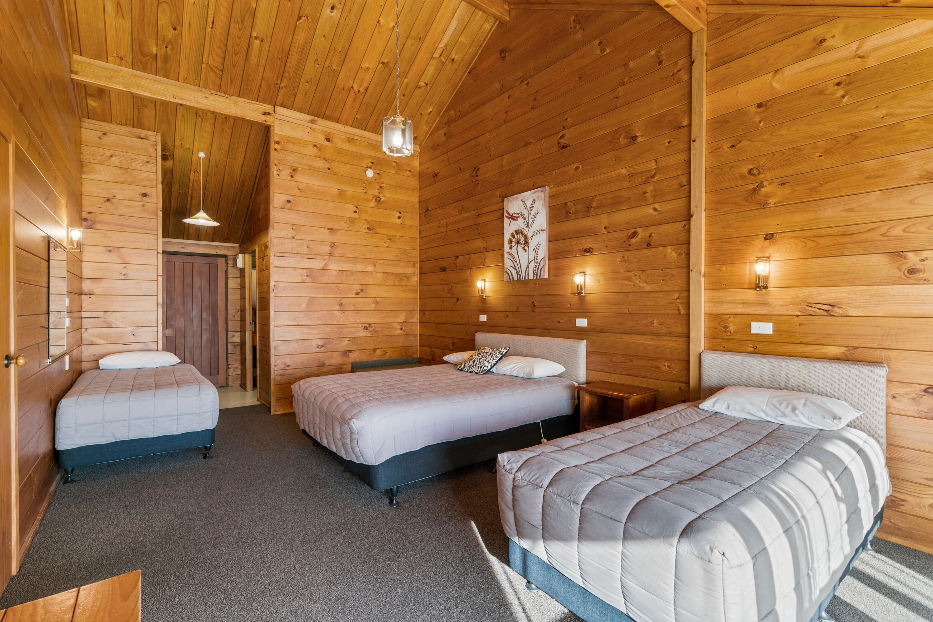 Una cabaña con tres camas, paredes de madera y una lámpara en el techo.