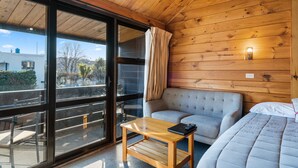 Een houten kamer met een slaapkamer, een bed, een tafel en een schuifdeur naar een buitenbalkon.