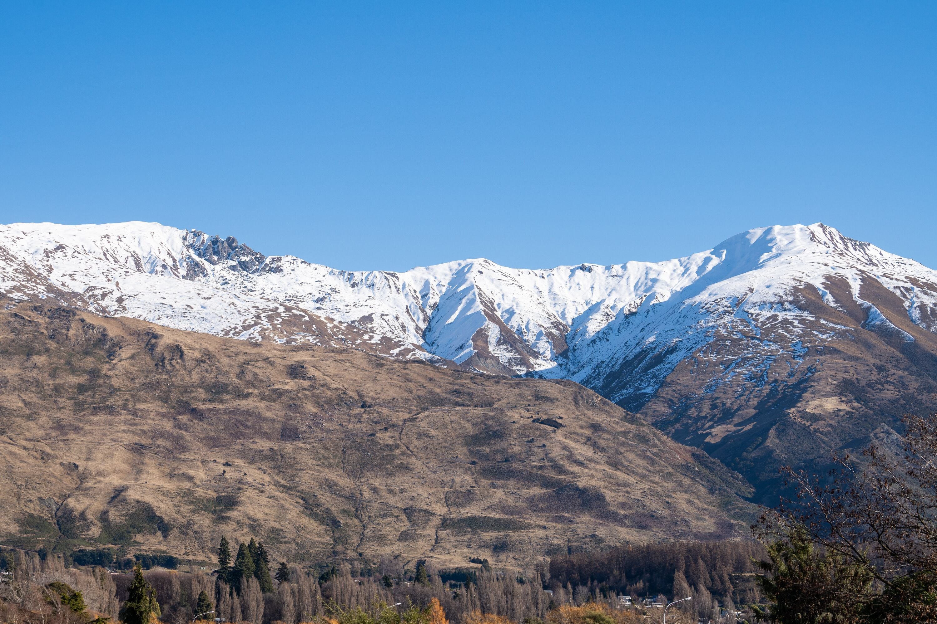 Eine Berglandschaft mit schneebedeckten Gipfeln und einem Tal mit kargen Pflanzen.