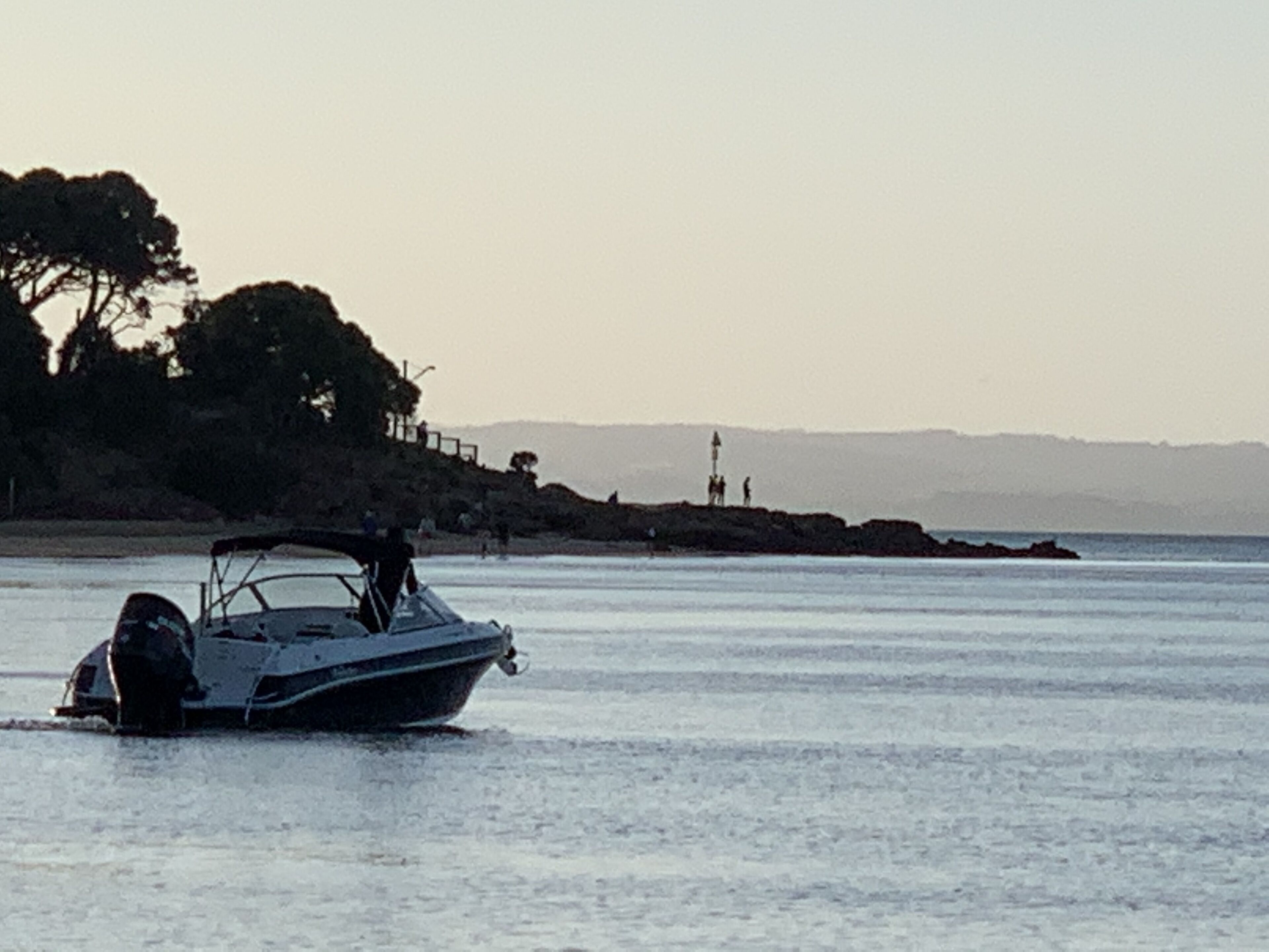 A boat on calm water near a rocky shore with a lighthouse in the distance.
