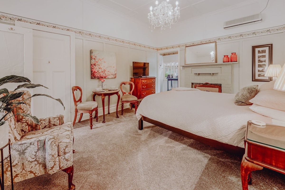 A bedroom with a large bed, a chandelier, a dresser, and a television.
