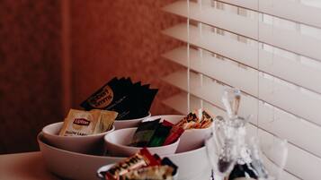 A table with bowls containing snacks and a bottle of wine, set against a window with blinds.