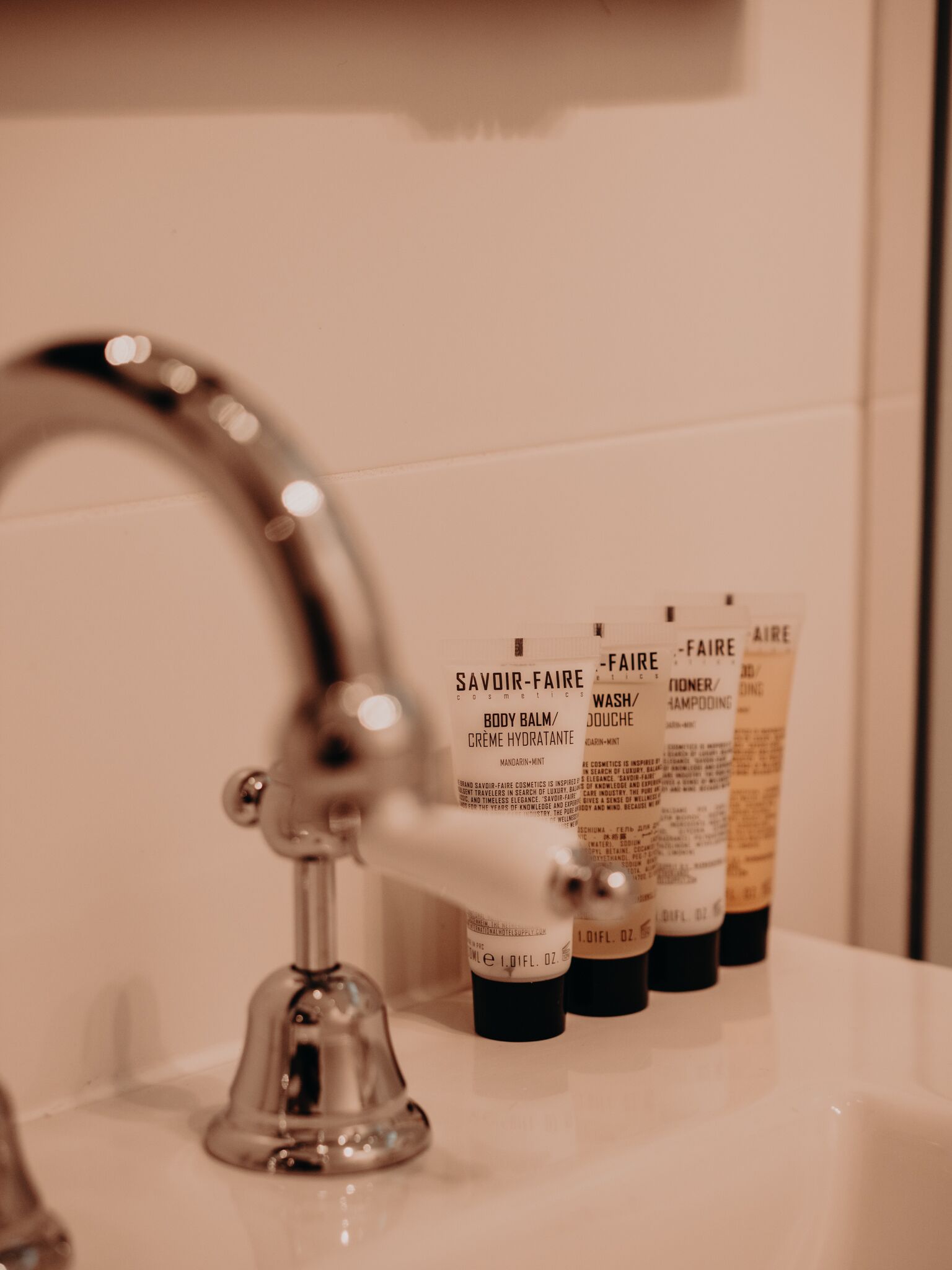 Un lavabo de salle de bain avec un robinet chromé et plusieurs flacons de produits de soins pour le corps de la marque Savour-Faire.