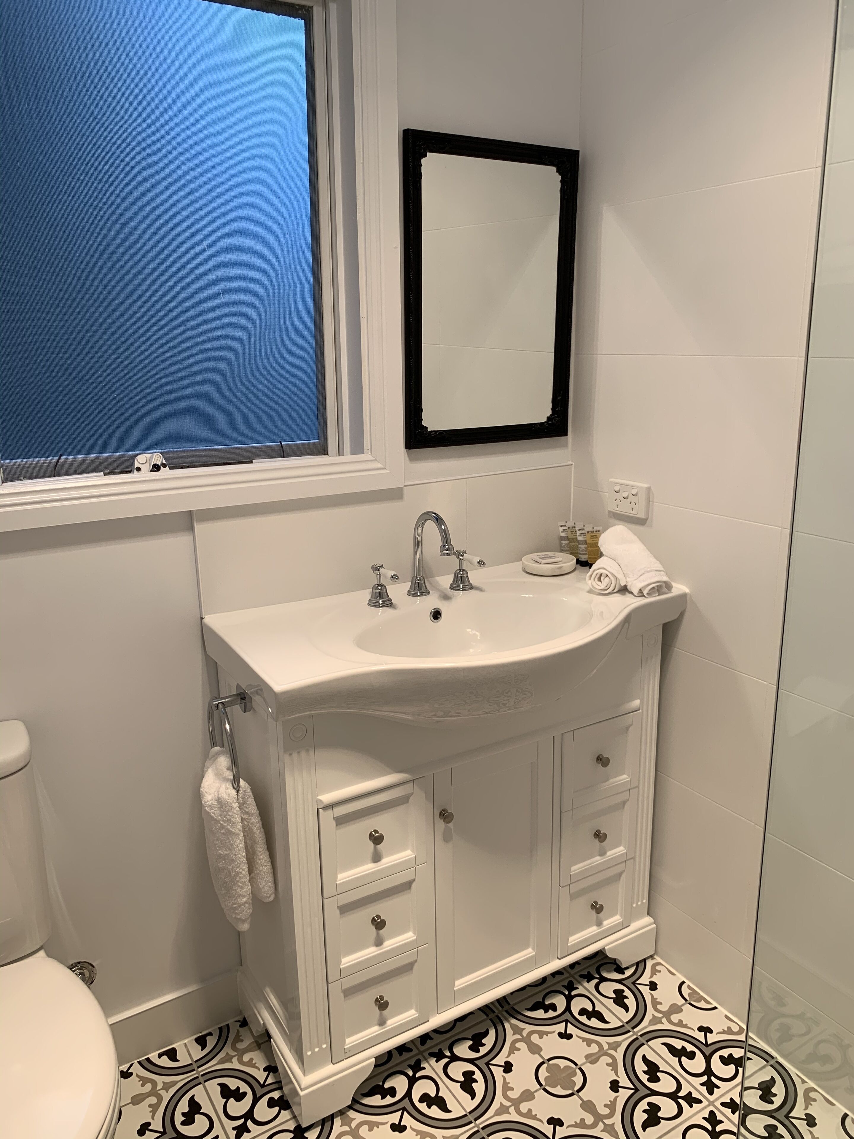 A bathroom with a white sink, a mirror above it, and patterned floor tiles.