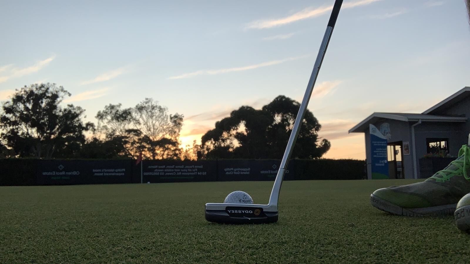 A golf club on a green with a building in the background.