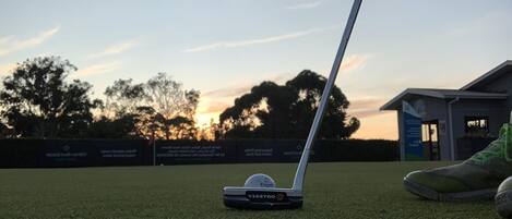 A golf club on a green with a building in the background.