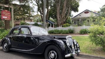 A vintage black car parked on a street with a sign for 'Genesta House Boutique Accommodation' and a 'VACANCY' sign.
