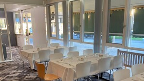 A dining area with tables set for service, large windows, and a patterned carpet.