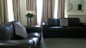 A living room with two black leather sofas, a vase with white flowers, and a clock on the wall.