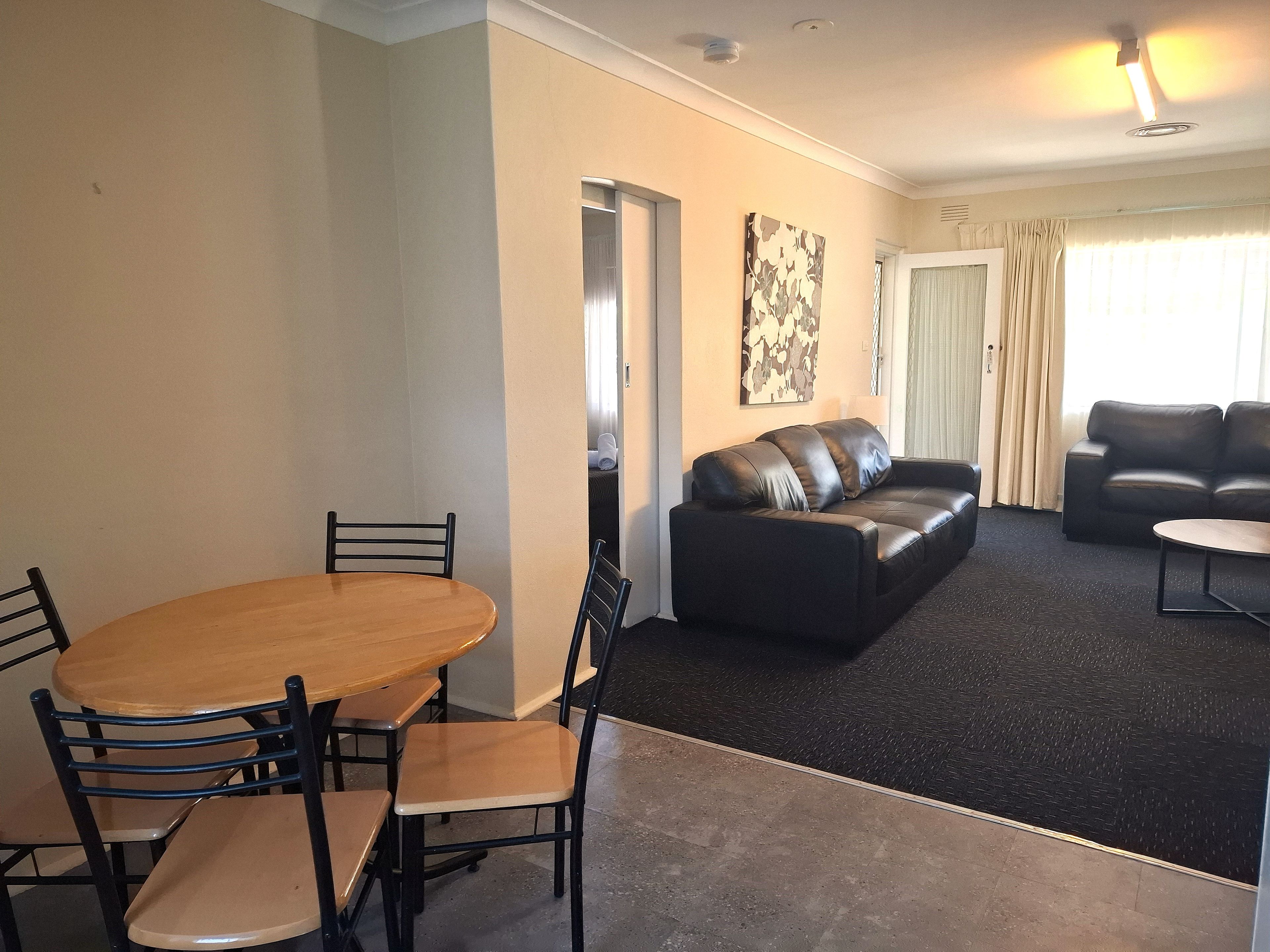 A living room with a black leather sofa, a wooden dining table with chairs, and a black coffee table.