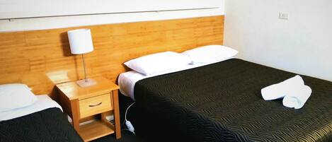 A hotel room with two single beds, a wooden headboard, a nightstand with a lamp, and a framed picture on the wall.