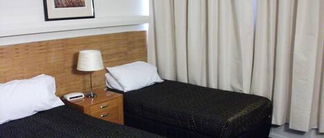 A hotel room with two beds, a nightstand with a lamp, a framed picture on the wall, and a window with curtains.