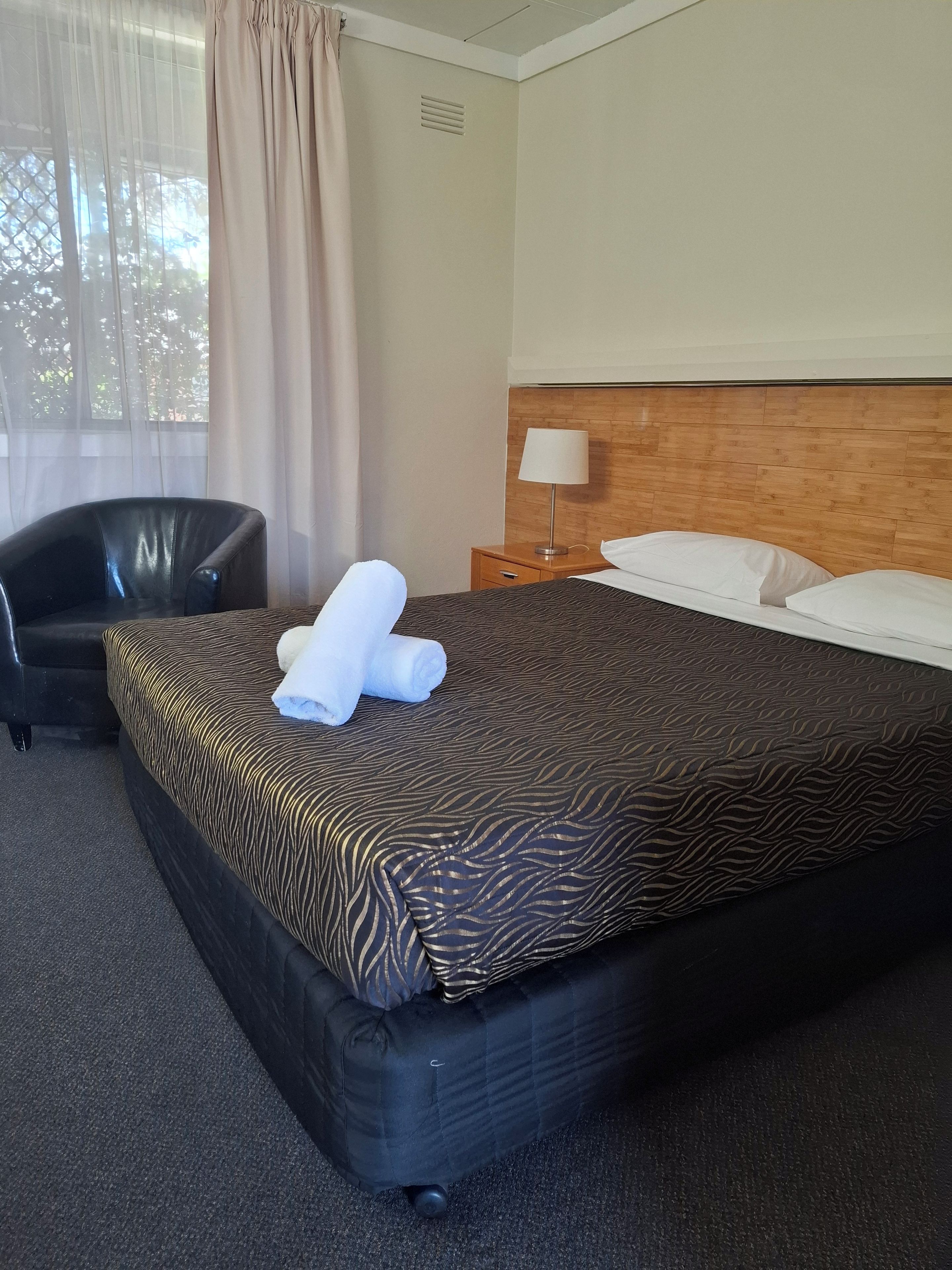 A hotel room with a bed, a chair, a nightstand, and a window with curtains.
