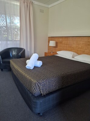 Una habitación de hotel con cama, una silla, una mesita de noche y una ventana con cortinas.