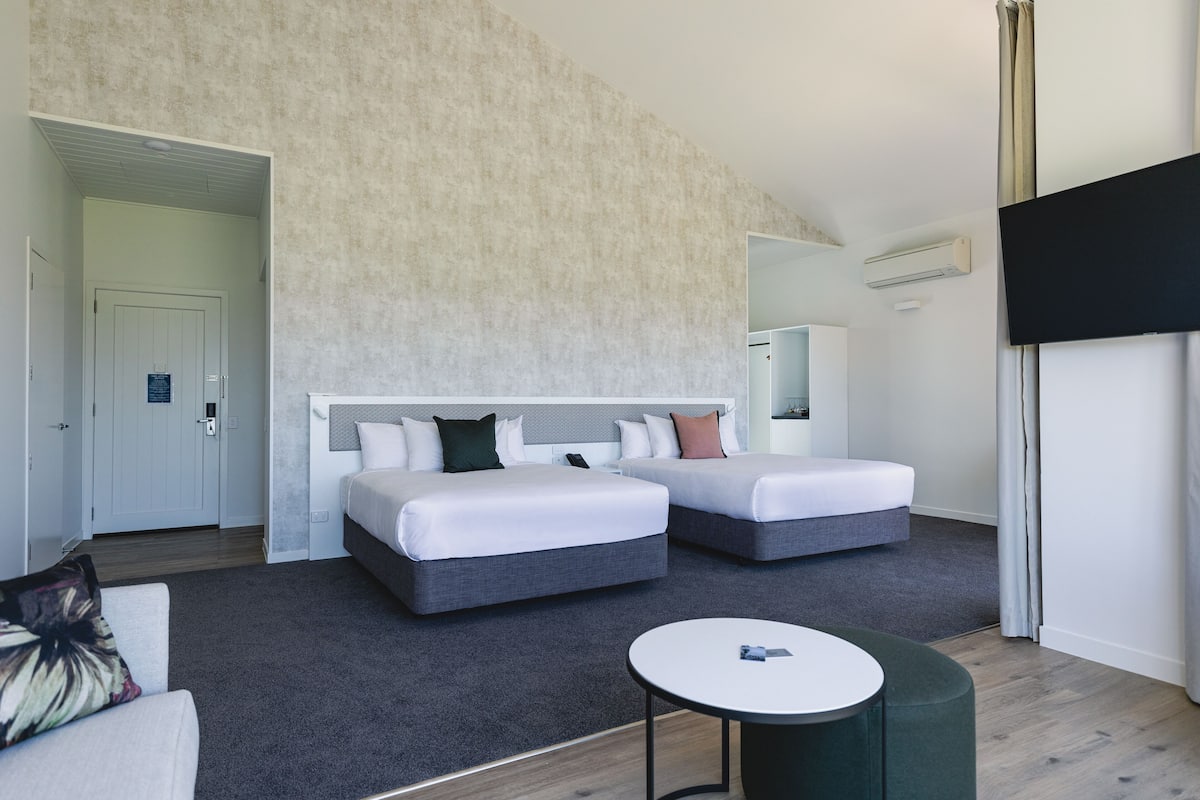 A modern hotel room with two beds, a small table, and a large window.