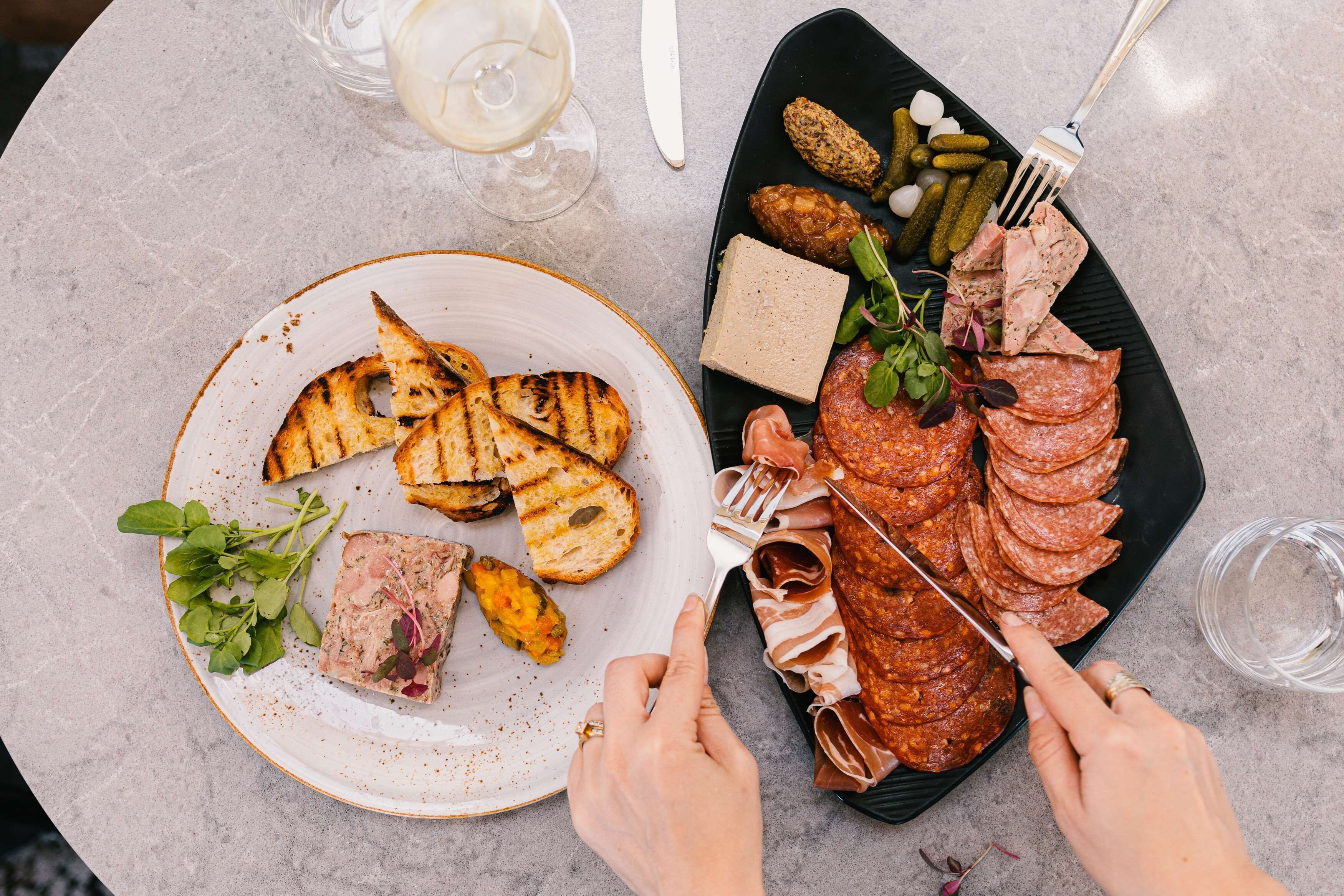 A table with a variety of food items including grilled fish, sliced meats, pickles, and bread.