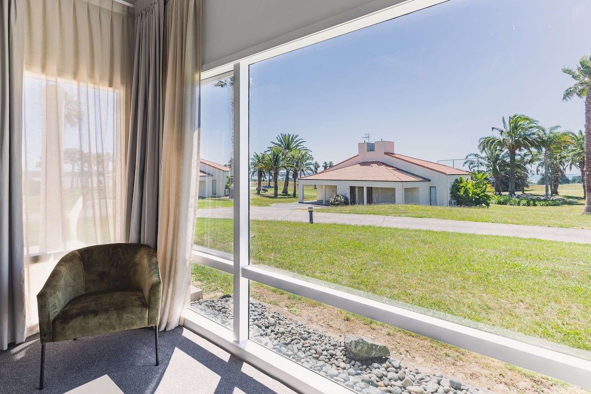 A room with a large window offering a view of a residential area with houses and palm trees.