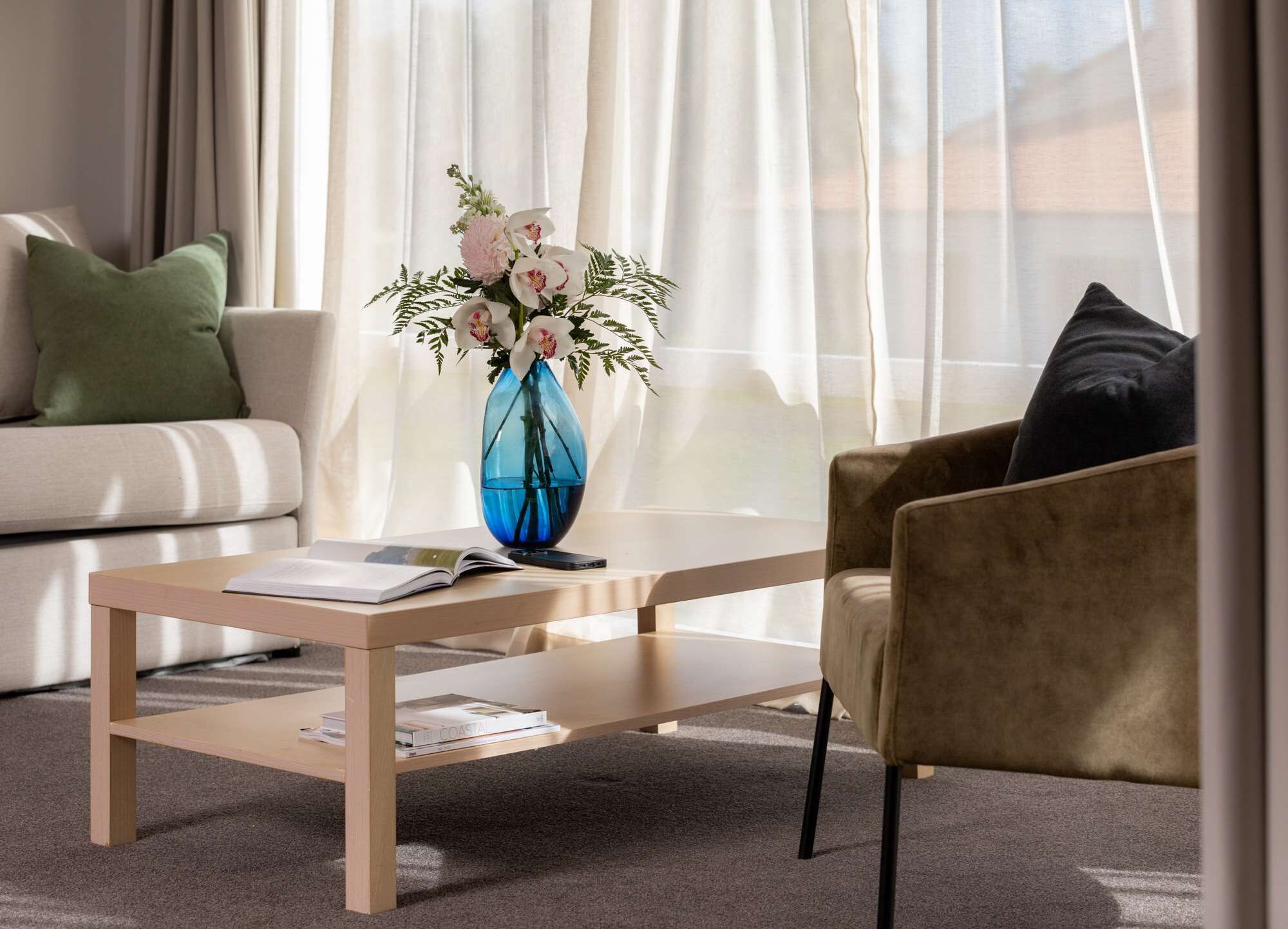 Una sala de estar moderna con un sofá, una mesa de centro y una silla. Un jarrón azul con flores está sobre la mesa de centro.