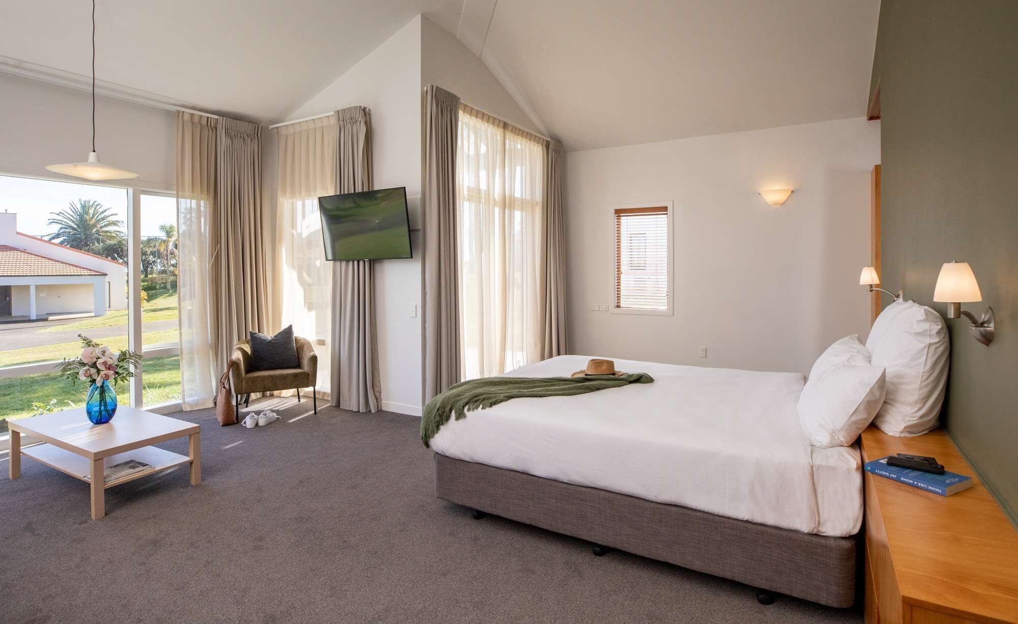 Habitación de hotel con cama, escritorio, silla, televisor y ventana con cortinas.