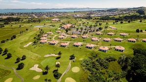 Vista aérea de un campo de golf con varios edificios, búnkeres de arena y una clara vista del paisaje circundante.