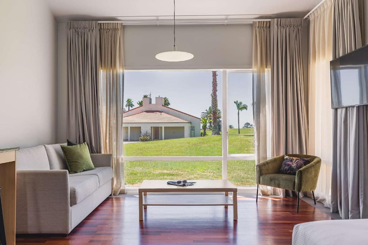 A modern living room with a large window, a sofa, a chair, and a coffee table.
