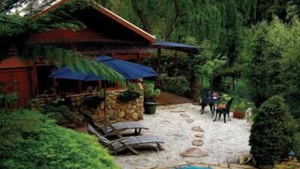 Un espacio al aire libre rústico con un patio de piedra, sillones de descanso, una piscina pequeña y una estructura de madera con techo de paja.