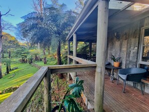 Una terraza de madera con mesa y sillas, con vistas a un paisaje verde y exuberante con árboles y cielo despejado.