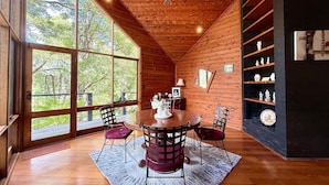 Interior de una cabaña de madera con una mesa de comedor, sillas y un ventilador de techo.