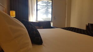 Una habitación de hotel con cama, lámpara, ventana y vistas a árboles, además de una puerta.
