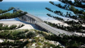 Una carretera costera con barandilla, playa y vista al océano.