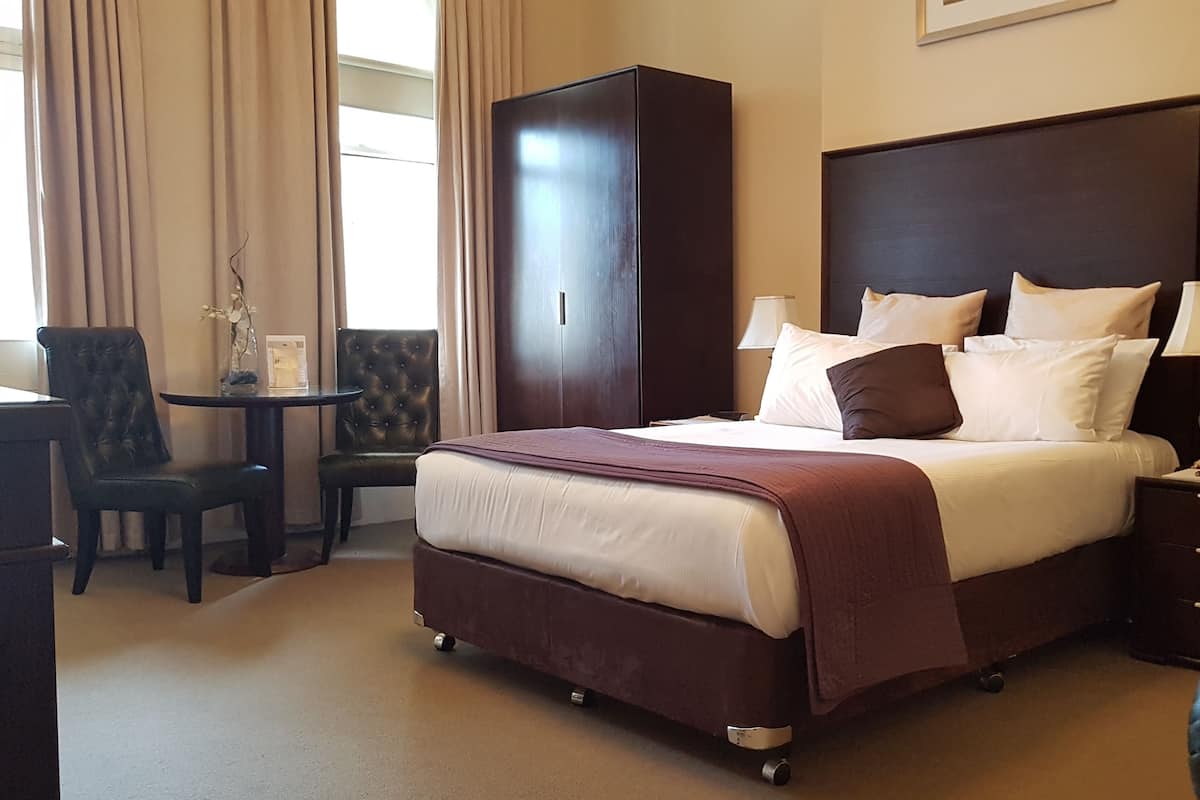A hotel room with a large bed, a desk, a chair, and a wardrobe.