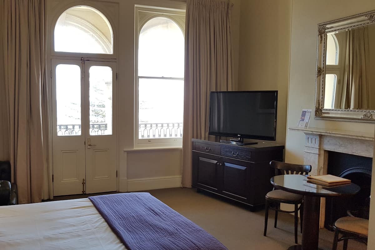 A hotel room with a bed, a TV, a desk with a chair, and a fireplace.