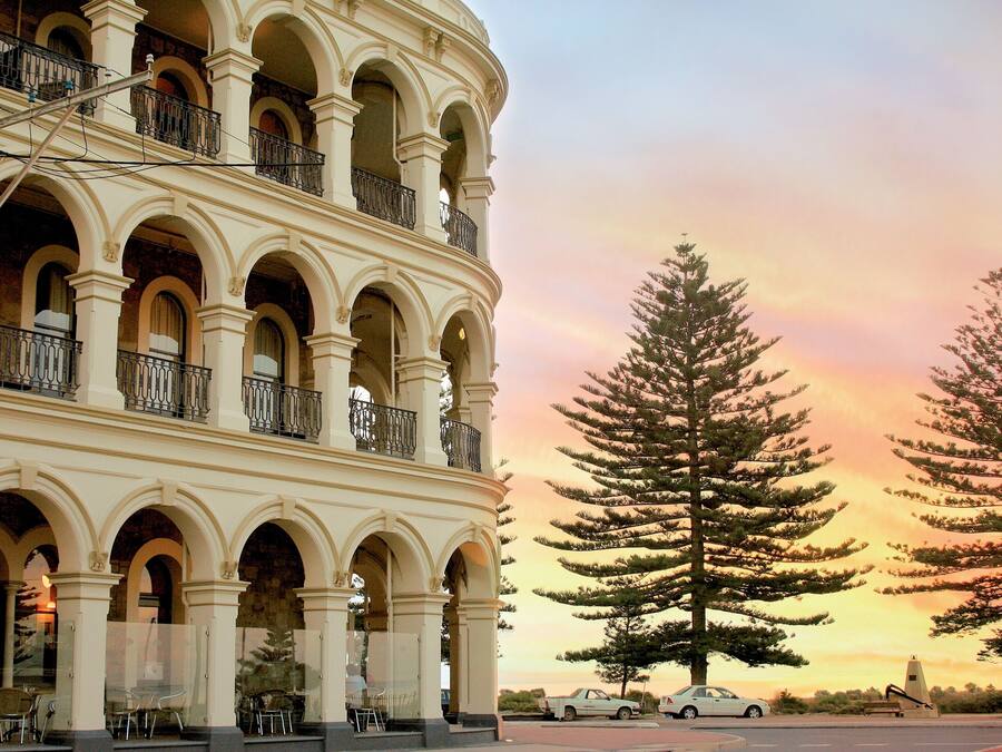 Edifici de diverses plantes amb estil arquitectònic clàssic, amb balcons arquejats i un arbre gran al davant.
