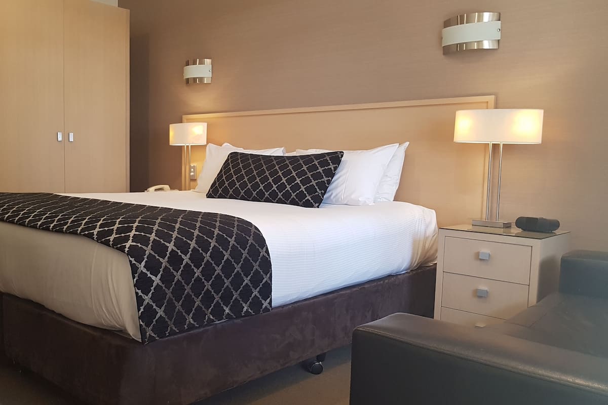 A hotel room with a large bed, bedside lamps, a desk, and a wardrobe.
