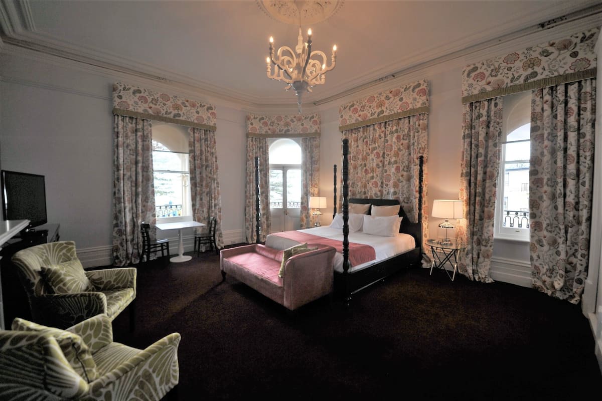 A four-poster bed with a pink bedspread, a chandelier, and floral curtains.