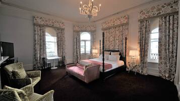 Ein Himmelbett mit einer rosa Bettdecke, einer Chandelierleuchtre und blumigen Vorhängen.