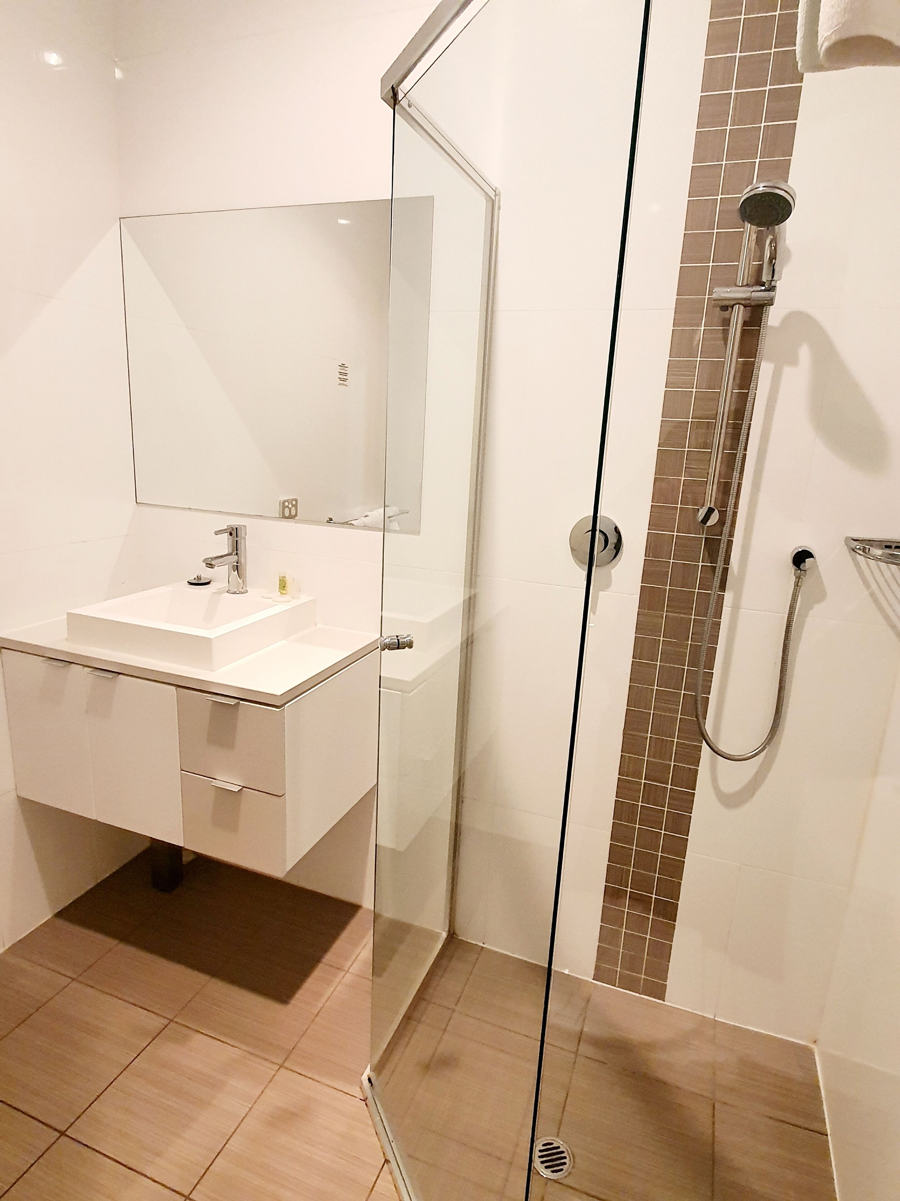 Un baño moderno con ducha acristalada, lavabo blanco y un espejo grande.
