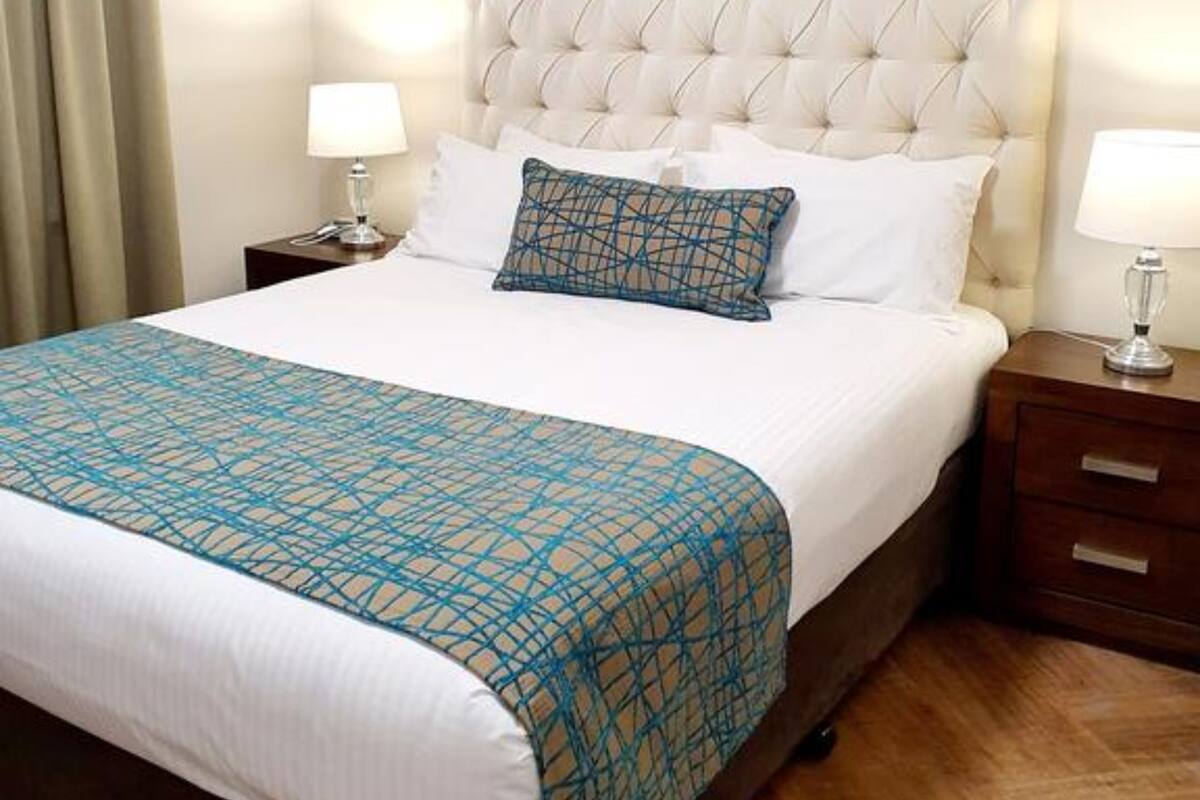 A neatly made bed with a patterned bedspread, two bedside lamps, and a wooden nightstand.