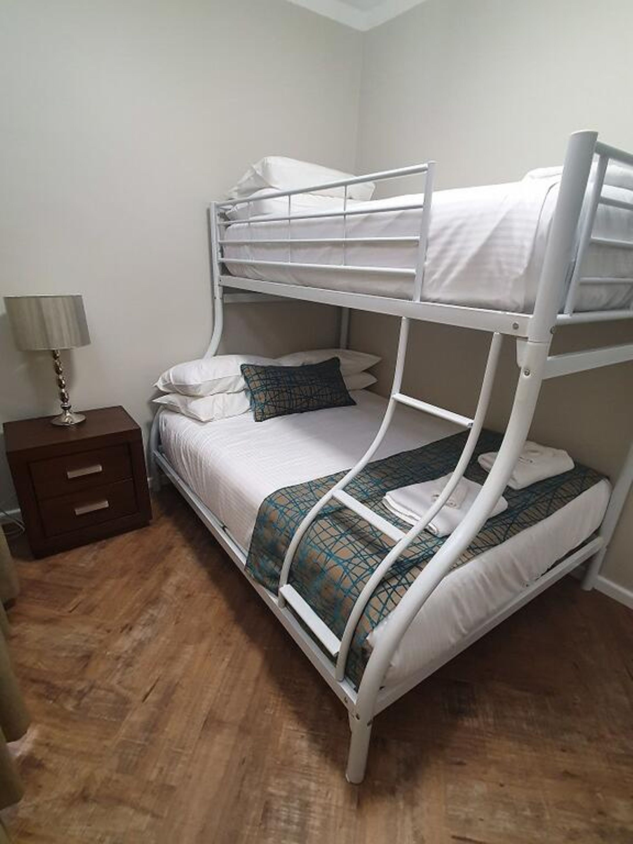 A bunk bed with a wooden nightstand and a lamp.