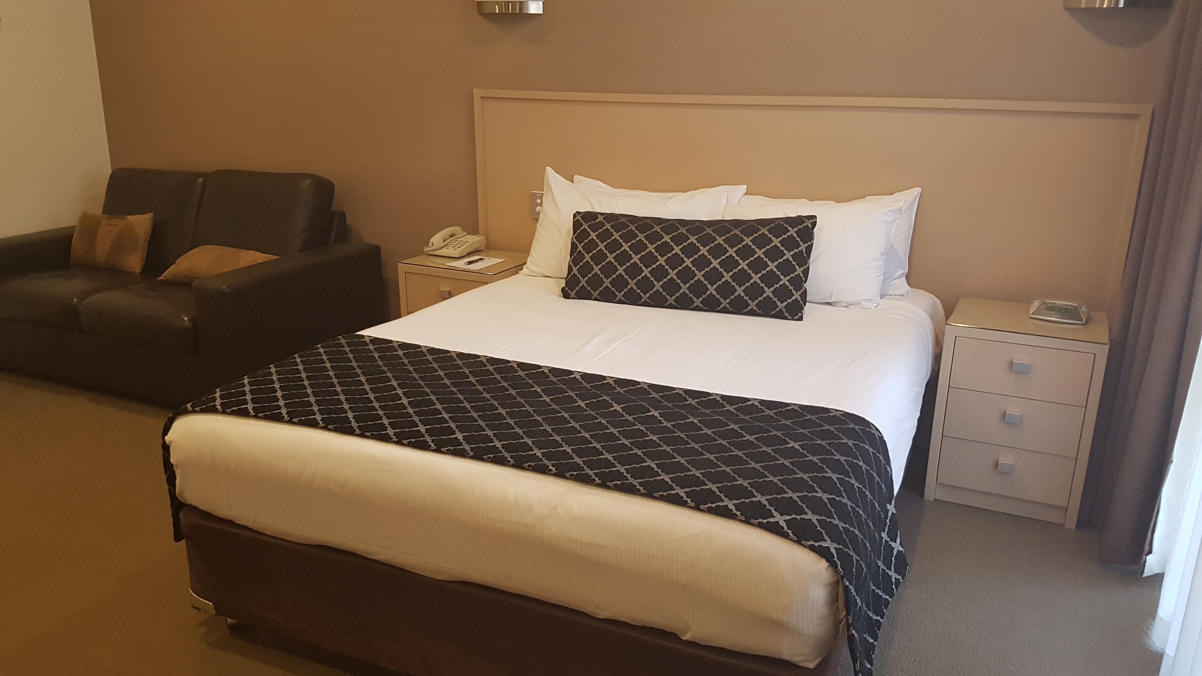Quarto de hotel com cama, mesa de cabeceira, cadeira e telefone.