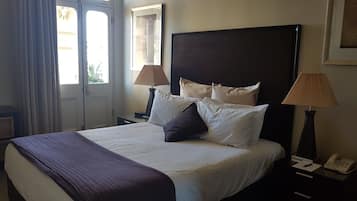 Quarto de hotel com uma cama grande, duas luminárias de cabeceira, mesa de cabeceira com telefone e uma janela com cortinas.