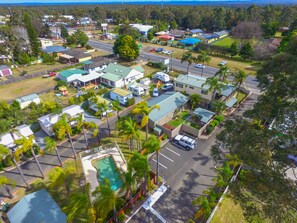 An aerial view of a residential area with multiple houses, a swimming pool, and a road. - Treehaven Tourist Park (Bomaderry)