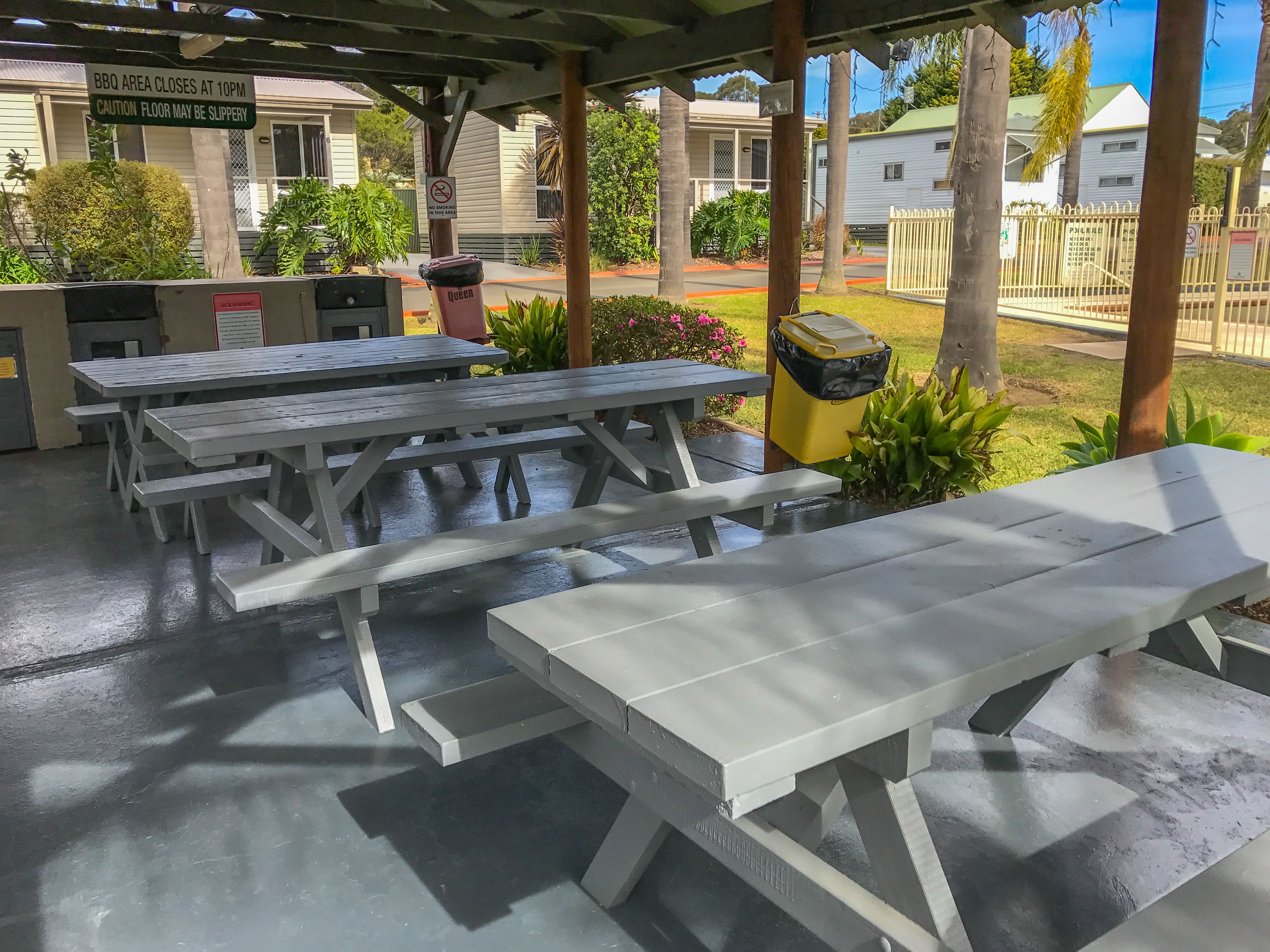 A covered outdoor area with picnic tables, a BBQ grill, and a sign indicating the BBQ area closes at 10 PM.