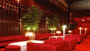 Een zitgedeelte in roodtinten met tafels en stoelen, bamboeplanten en sfeerverlichting.