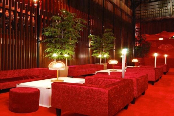 Un área de estar con temática roja, con mesas y sillas, plantas de bambú e iluminación ambiental.