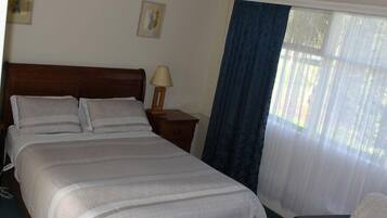 A neatly made bed with a wooden headboard, a bedside table with a lamp, and a window with blue curtains.