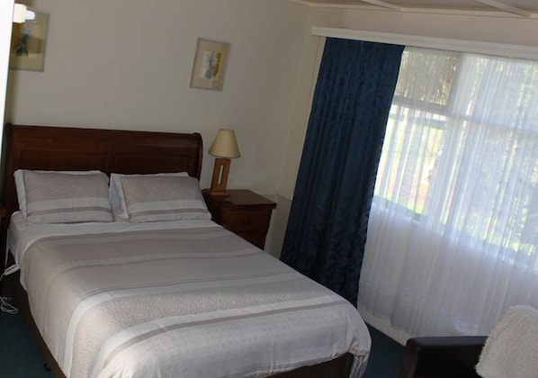 A neatly made bed with a wooden headboard, a bedside table with a lamp, and a window with blue curtains.