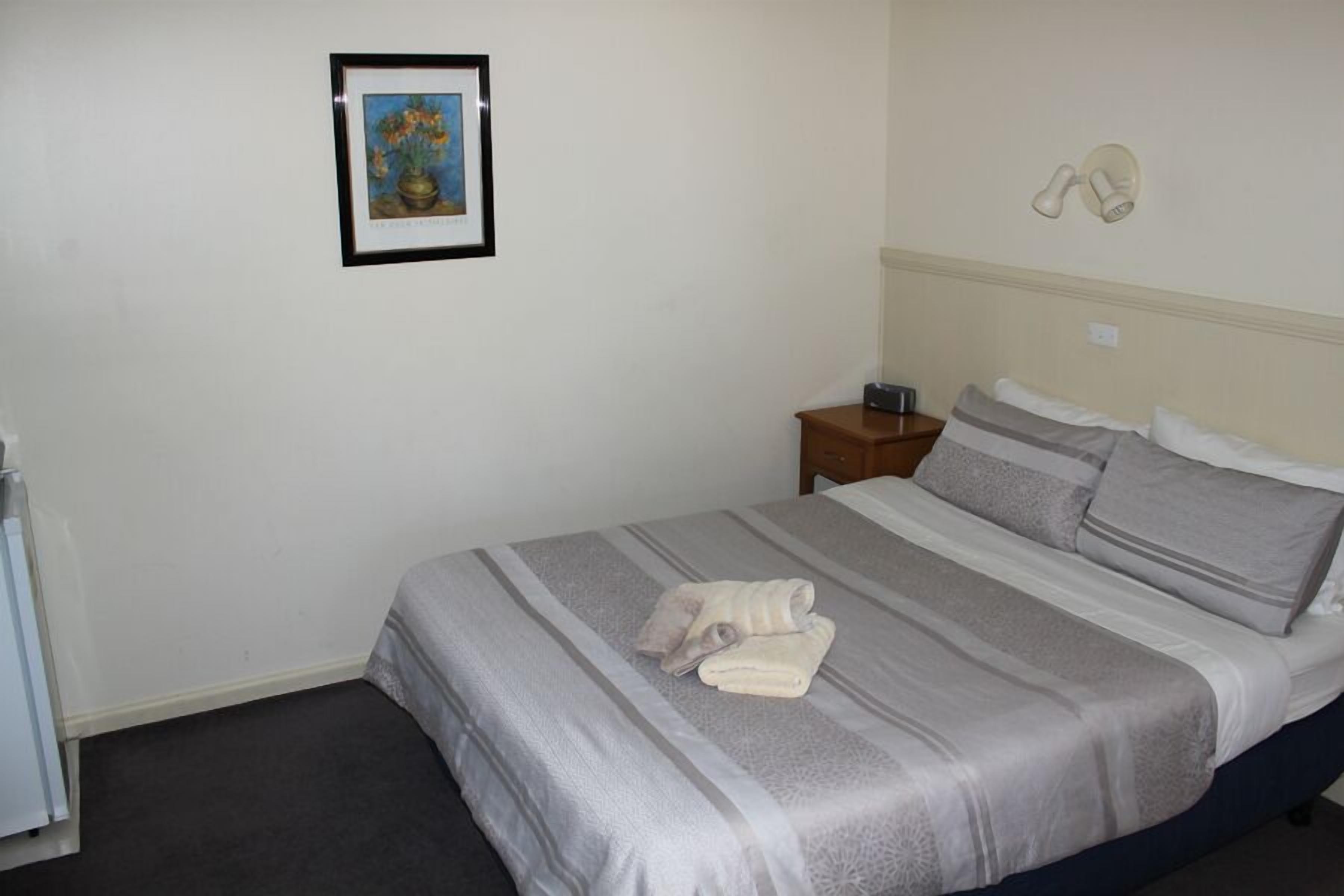 Ein ordentlich bezogenes Bett mit gestreifter Tagesdecke und Kissen, ein gerahmtes Bild an der Wand und ein Nachttisch mit Lampe.