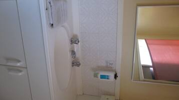 Un pequeño espacio de ducha cerrado con un muro de azulejos blancos, una toalla colgada en la pared y un inodoro con dispensador de toallas de papel.